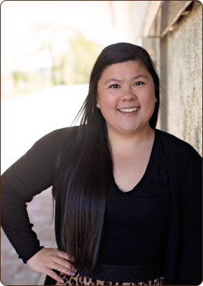 A young woman with long, dark hair smiles at the camera, with one hand on her hip.