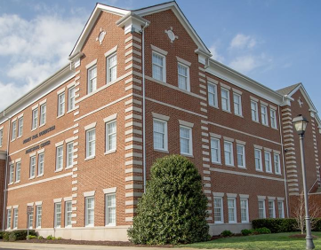 A multi-story brick building with many windows and a large green bush in front.