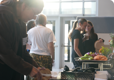 People gather around tables with food and drinks in an event space.