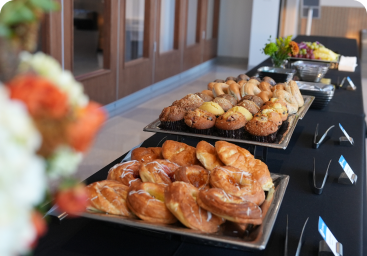 A close-up of a breakfast buffet table laden with trays of muffins and pastries.
